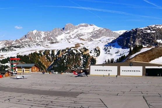 Petits avions devant les hangars de l’altiport de Courchevel, au pied de montagnes enneigées.